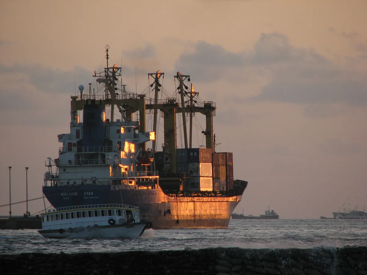 Container cargo ship Maldive Star at sunset with a passenger ferry in front