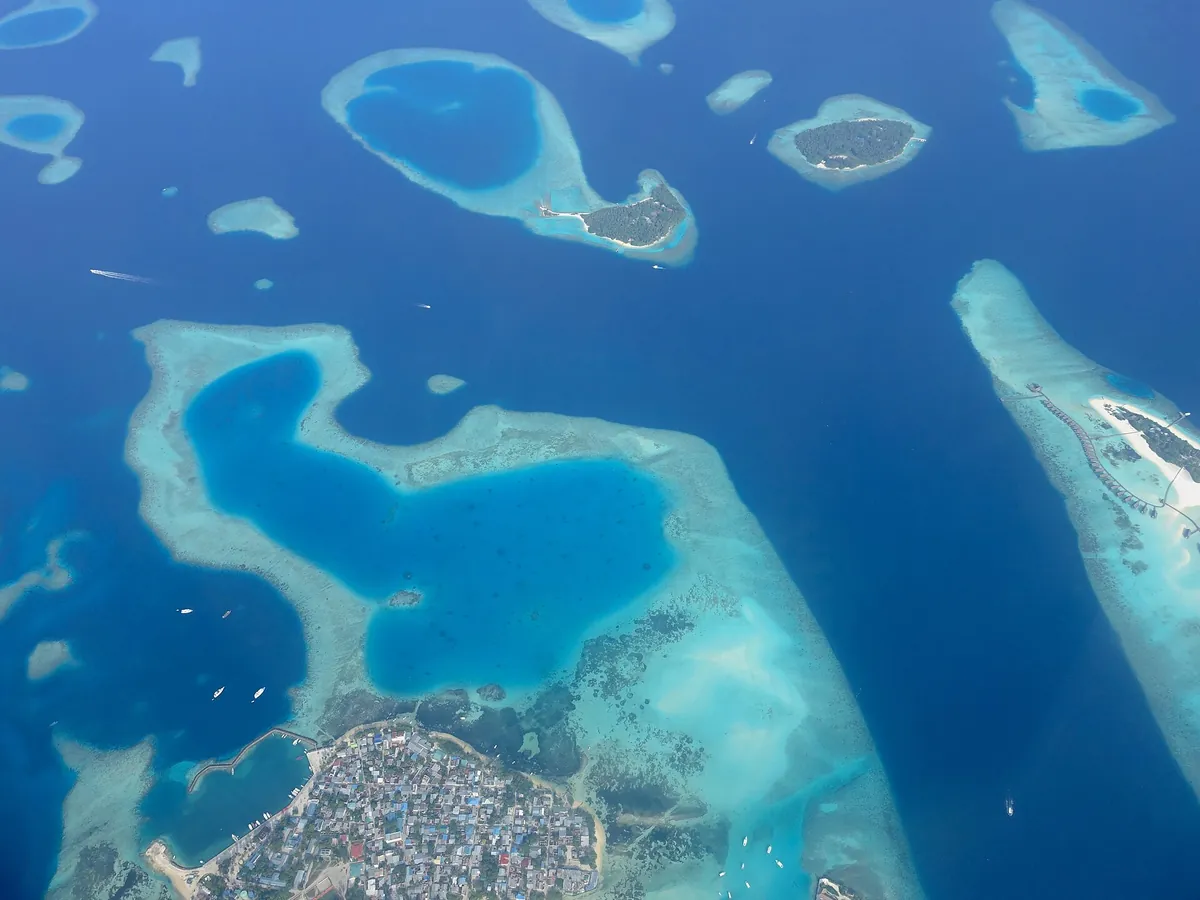 Aerial view of turquoise reefs and the inhabited island of Guraidhoo in Kaafu Atoll